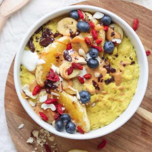 Overhead photograph of golden vegan oatmeal with caramelised bananas, oranges and blueberries, with more blueberries and a round chopping board in the background