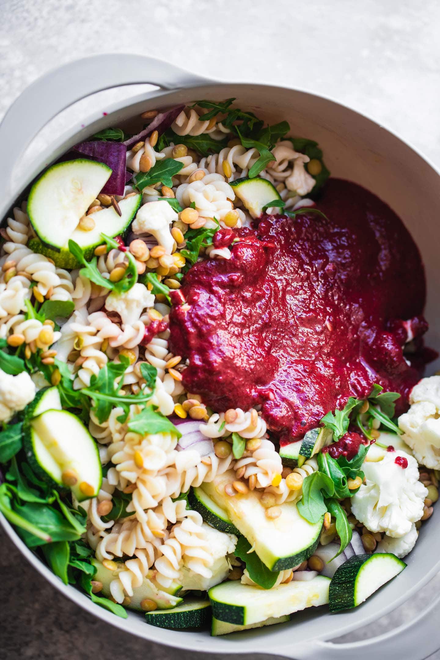 Pasta and vegetables in a mixing bowl with a beetroot sauce