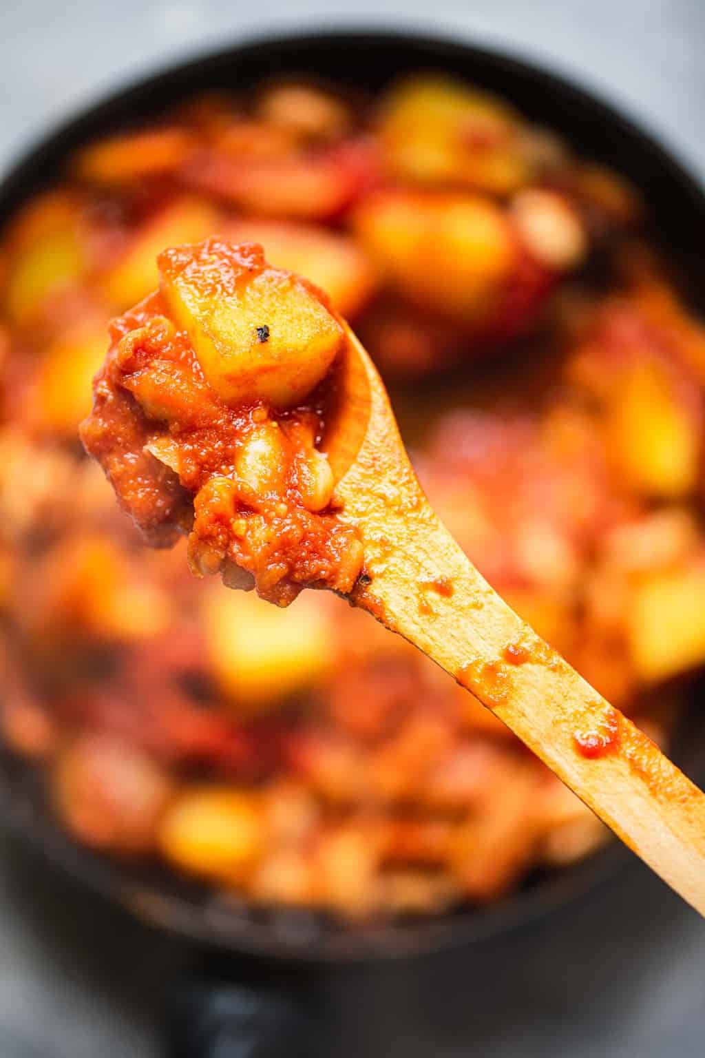 Closeup of spoon with potatoes and beans in a tomato sauce