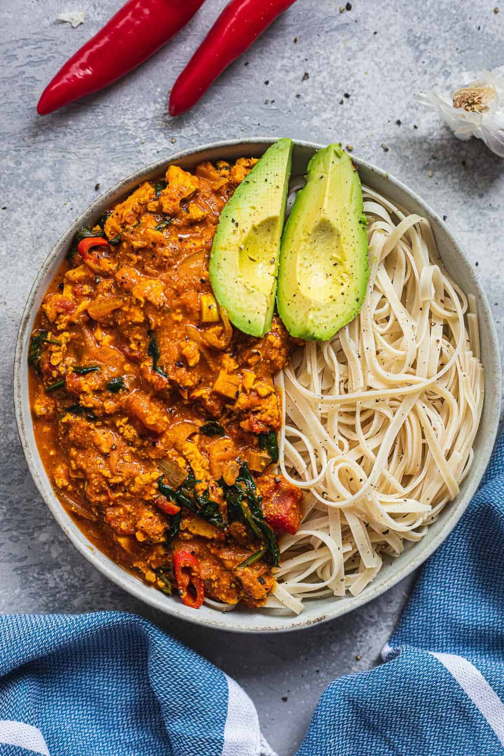 Curry with spinach and tofu in a bowl with noodles and avocado