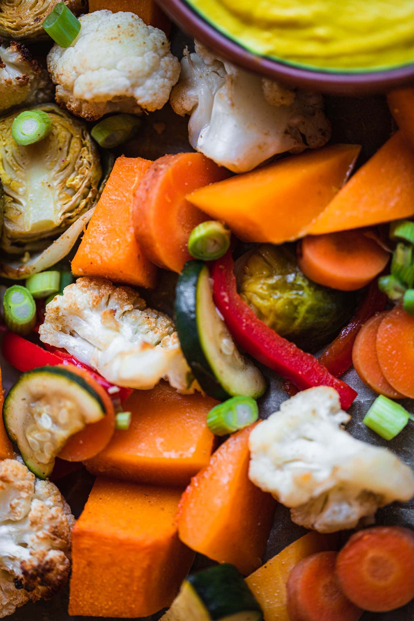 Closeup of Brussels sprouts, butternut squash, cauliflower, carrots, red bell peppers and zucchini on a baking tray