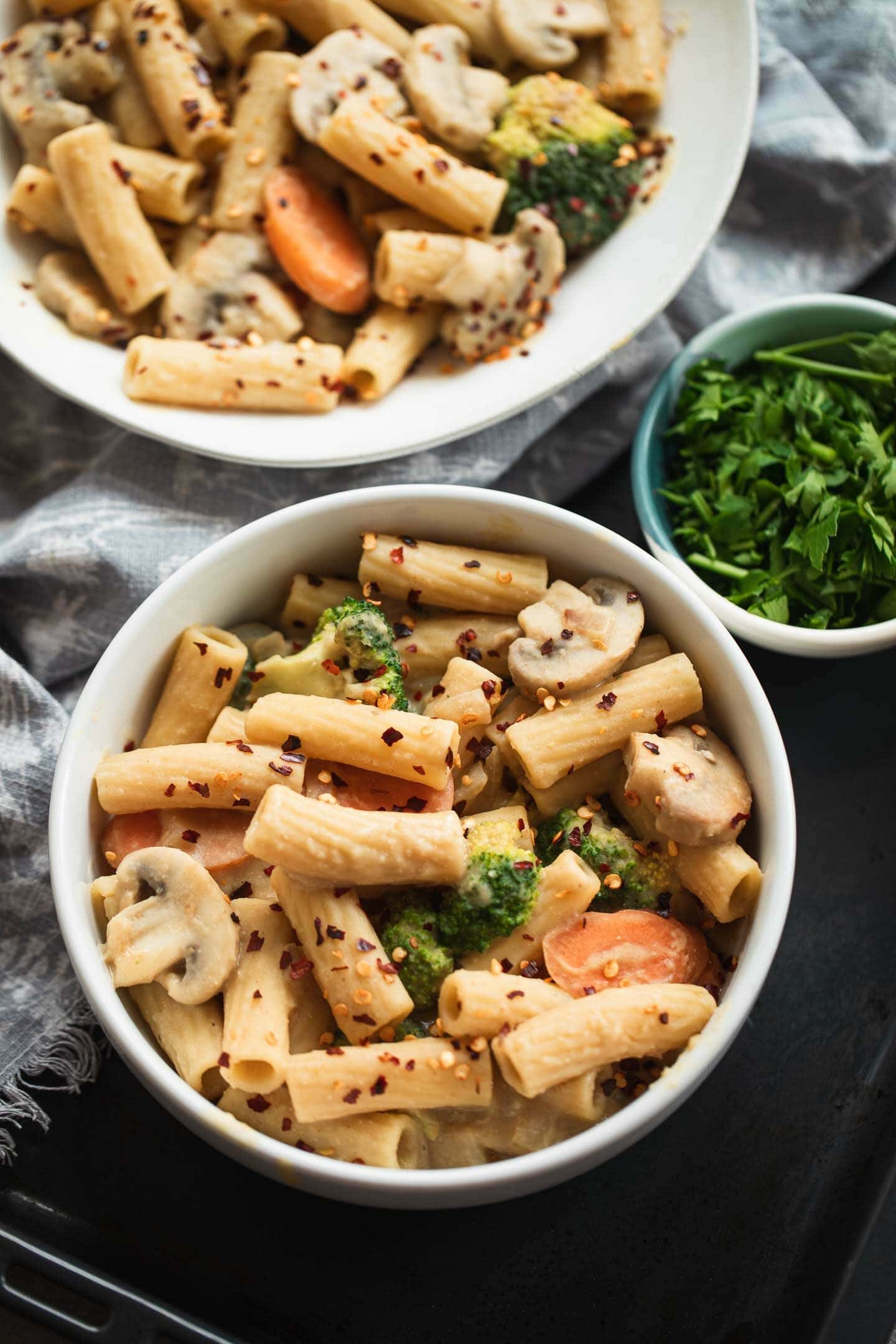 Two bowls of vegan pasta with broccoli, vegetables and a creamy sauce