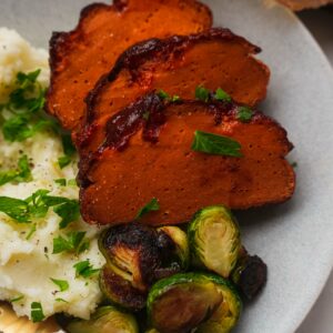 Vegan ham on a plate with mashed potatoes and Brussels sprouts